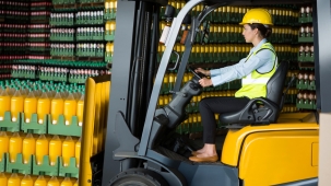 Side view of confident female worker driving forklift in warehouse