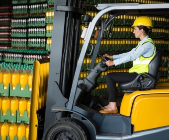 Side view of confident female worker driving forklift in warehouse