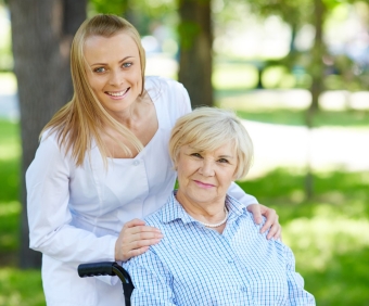 Pretty nurse and senior patient in a wheelchair looking at camera in park