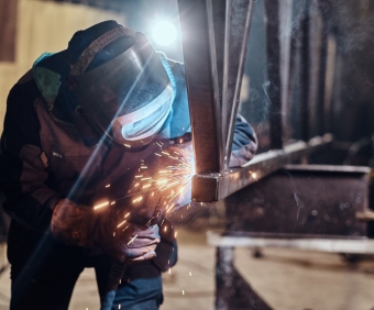 Man is working at metal factory, he is welding a piece of rail using special tools.
